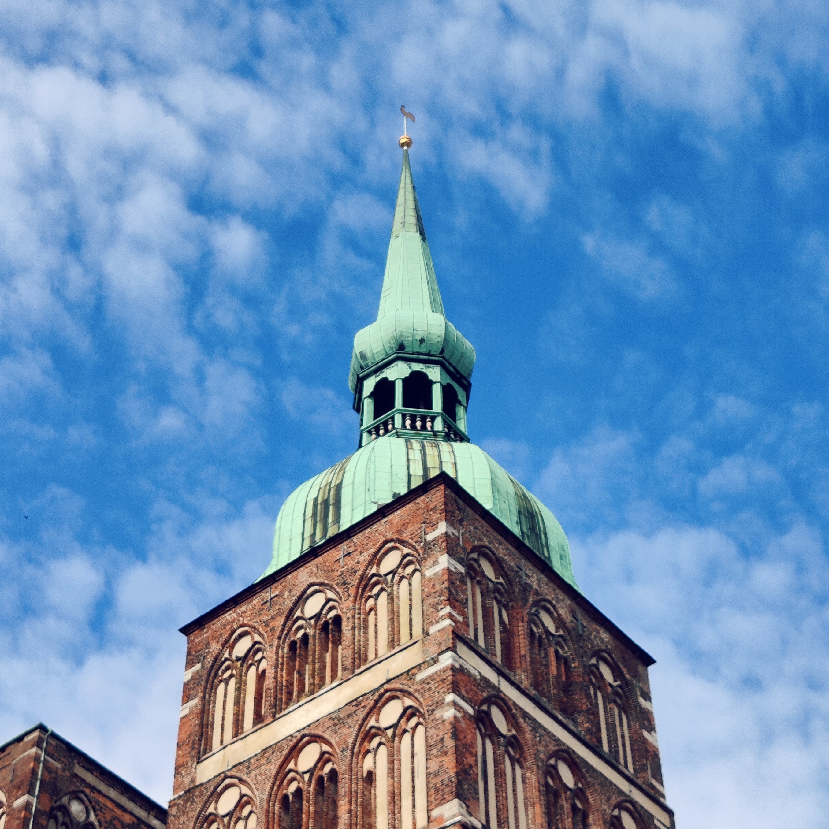 photo of St. Nicholas Chorch in Stralsund, showing the tower in front of a blue sky with some fluffy clouds